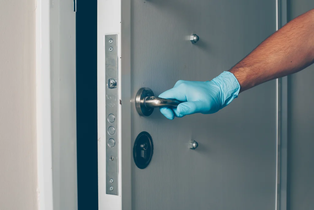 Mano con guante azul abriendo una puerta para inspección y mantenimiento de la cerradura